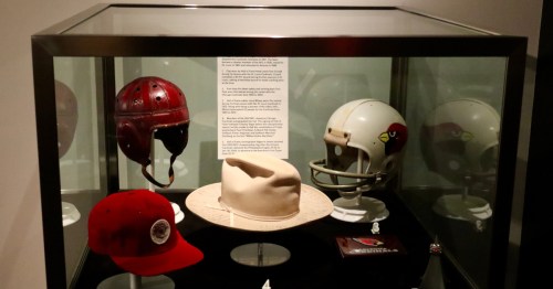 Historical Arizona Cardinals leather and modern helmets inside a glass display case at the Canton NFL museum.