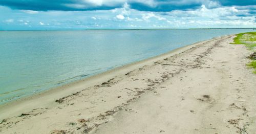 Views of Holly Beach, a hidden beach in Louisiana, featuring an empty sandy shore and calm blue waters.