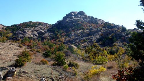 A rocky hill surrounded by autumn foliage under a clear blue sky.
