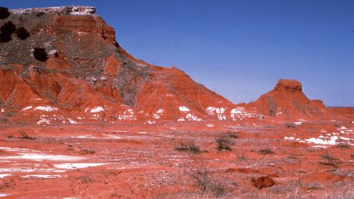 A vibrant red rock formation under a clear blue sky, with sparse vegetation in the foreground.