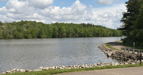 A rocky shoreline and paved walking path curving along the water at Stonelick State Park, Ohio.