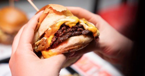 hands holding a smashburger with melted cheese and grilled onions