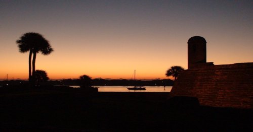 Spooky sunset view as seen from St. Augustine, Florida, with historic building and palm trees in silhouette.