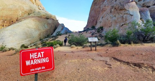 Views of a red and white heat warning sign at the entrance of a trail at Valley of Fire State Park in NV.